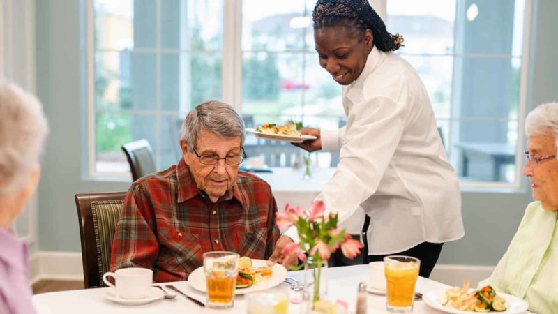 Dining staff serving senior man seated at table